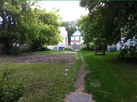 a path runs through a wooded area beside an in-ground garden